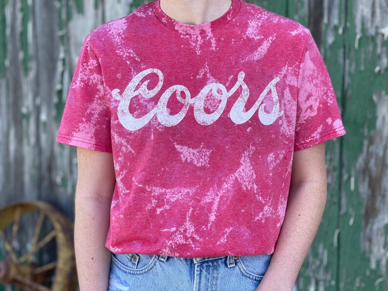 May include: Red t-shirt with a white bleach tie-dye pattern and the word "Coors" printed in white.