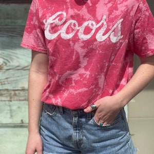 May include: A pink tie-dye t-shirt with the word "Coors" in white lettering.
