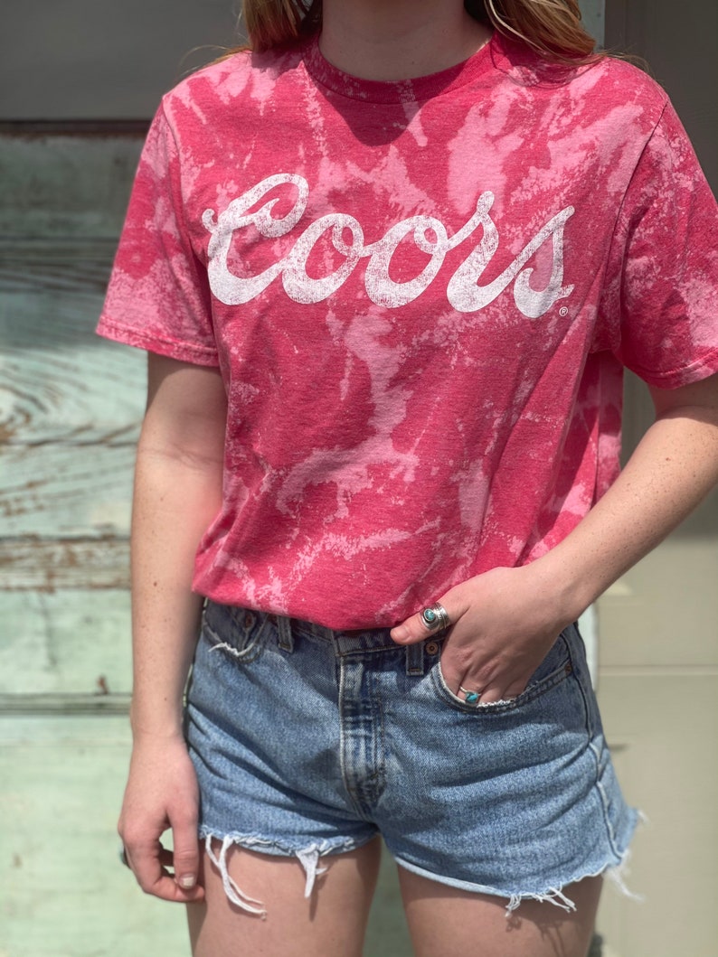 May include: A pink tie-dye t-shirt with the word "Coors" in white lettering.
