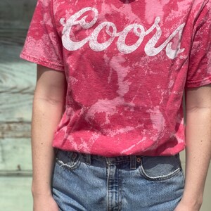 May include: A pink tie-dye t-shirt with the word "Coors" in white lettering.