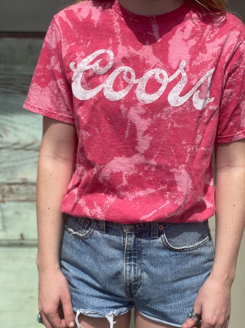 May include: A pink tie-dye t-shirt with the word "Coors" in white lettering.