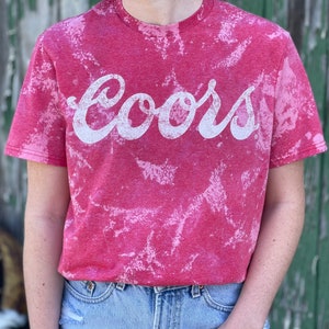 May include: Red t-shirt with a white bleach-splattered design and the word "Coors" in white lettering.