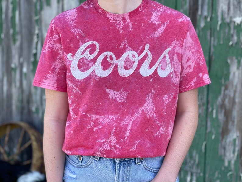 May include: Red t-shirt with a white bleach-splattered design and the word "Coors" in white lettering.