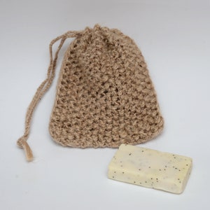 May include: A brown crocheted drawstring bag made of natural fibers, with a white bar of soap with black specks inside.