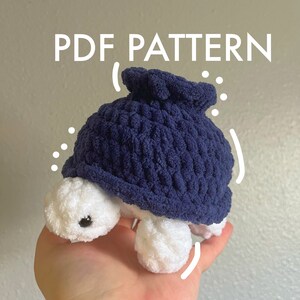 May include: A PDF pattern for crocheting a small, blue and white turtle toy. The turtle is sitting in a hand, with its head and legs visible.