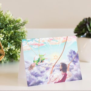 Puede incluir: Una tarjeta de felicitación con una pintura de un hombre y una mujer en un columpio en las nubes. El hombre lleva una túnica roja y la mujer lleva un vestido verde. El cielo es azul con nubes blancas y el sol brilla.