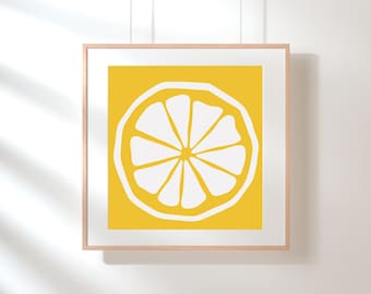 May include: A framed print featuring a stylized illustration of a lemon slice. The artwork has a bright yellow background with a white lemon slice design. The print is in a light-colored wooden frame, suitable for kitchen or dining room decor.