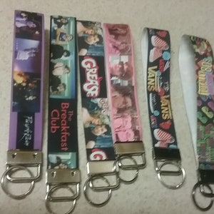 May include: Six colorful keychains with different designs. The keychains feature images of the Breakfast Club, Grease, Vans, and the 80s. The keychains are all attached to silver key rings.