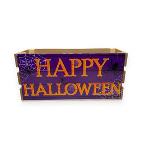 May include: A wooden crate with a purple background and the words "Happy Halloween" in orange letters. The crate is decorated with black spiders and white spiderwebs.