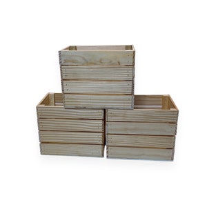 May include: Three unfinished wooden crates stacked in a pyramid formation. The crates are made of light-colored wood, with horizontal slats and visible nail heads. The boxes are empty and have a square shape.