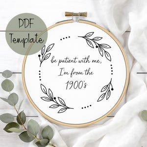 May include: A white fabric stretched within a wooden embroidery hoop, featuring the text "be patient with me, I'm from the 1900's" in a handwritten style. The text is surrounded by a black floral design. A green circle with the text "PDF Template" is in the upper left corner.