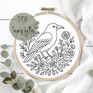 May include: A black and white embroidery hoop featuring a crow design surrounded by flowers and foliage. The text "PDF Template" is visible on the upper left. The embroidery is set in a wooden hoop.