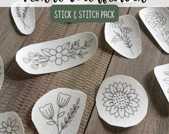May include: A collection of white fabric stick and stitch embroidery patches featuring black line art of various wildflowers, including a sunflower, tulips, and daisies, with the text Floral Wildflower STICK & STITCH PACK.