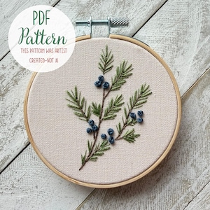 May include: An embroidery hoop containing light beige fabric with a hand-stitched design of a green pine branch featuring dark blue berries. The text on the image reads: PDF Pattern, This pattern was artist created-not AI.