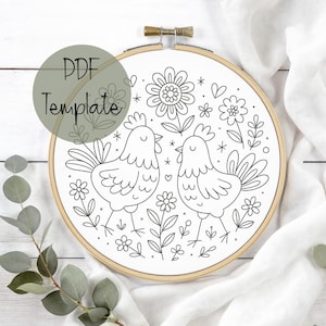 May include: A black and white embroidery hoop featuring a floral and chicken design. The design includes two chickens, flowers, and the text "PDF Template" in a green circle. The hoop is set in a wooden frame.