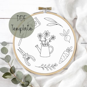 May include: A wooden embroidery hoop with a white fabric background features a black and white line drawing of gardening tools and elements. The design includes a watering can with flowers, a packet of seeds, and a carrot. The text "PDF Template" is also present.