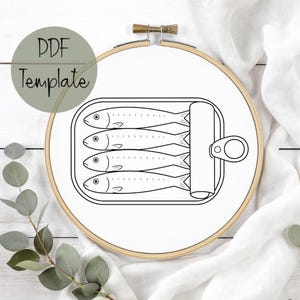 May include: A black and white line drawing of sardines in a can, displayed within an embroidery hoop. The text "PDF Template" is in a green circle in the upper left corner. The hoop is set against a white background.