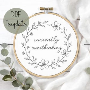 Könnte beinhalten: Ein weißes Stoffstück in einem hölzernen Stickrahmen mit einem floralen Kranzdesign. Der Text "currently overthinking" ist mittig platziert. Ein grüner Kreis mit dem Text "PDF Template" befindet sich oben links.