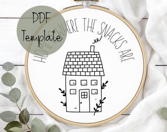 May include: A wooden embroidery hoop with a white fabric featuring a black line drawing of a house and the text "WHERE THE SNACKS ARE". The words "PDF Template" and "HOME" are also visible.