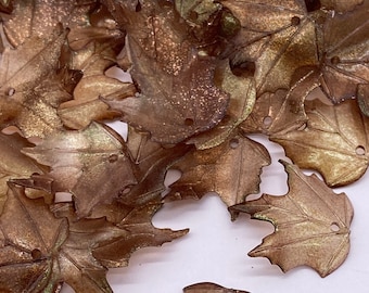May include: A pile of brown and green maple leaf shaped charms with a US penny for scale.