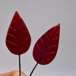 Può includere: Due foglie di vetro rosso con una texture venata su sottili steli di filo.