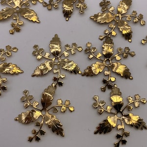 May include: Eight gold metal floral embellishments with a delicate, intricate design. Each embellishment features a central circle surrounded by multiple leaf-like shapes.