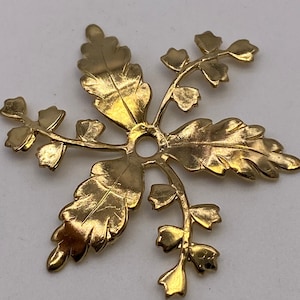 May include: Gold-toned metal pendant with a floral design. The pendant features a central hole and five branches with leaves and small flowers.