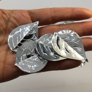 以下が含まれることがあります： 葉の形をした銀色の金属製の装飾品で、細かい葉脈模様が施されています。葉の長さは約5cmで、光沢のある仕上げになっています。