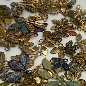 May include: A collection of metal leaf charms in various colors, including gold, silver, green, blue, and black. The charms have a delicate, intricate design and are perfect for adding a touch of whimsy to jewelry or crafts.
