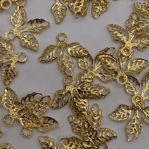 May include: Gold-toned metal leaf-shaped charms with a loop at the top. The charms are intricately designed with a delicate, lacy pattern.