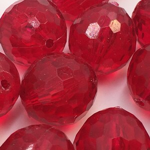 May include: A group of red faceted glass beads. The beads are round and have a shiny finish.
