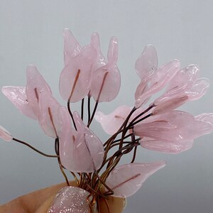 May include: A bunch of pink glass flower petals attached to thin copper wires. The petals are translucent and have a delicate, feminine appearance.