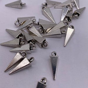 May include: A group of silver triangle-shaped charms with a loop at the top. The charms are scattered on a white surface.