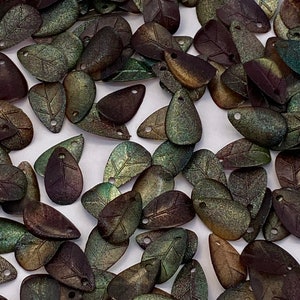 Könnte beinhalten: Eine Sammlung von schimmernden, grün-braunen, blattförmigen Perlen mit einem Loch oben. Die Perlen haben eine strukturierte Oberfläche und einen dezenten Metallic-Glanz.