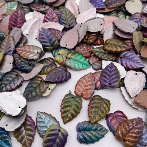 May include: A collection of iridescent leaf-shaped charms with a hole in the center. The charms are made of a metallic material and have a variety of colors, including green, blue, purple, and orange.