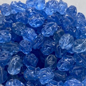 Puede incluir: Un montón de cuentas de vidrio azul translúcido con una forma ligeramente irregular y facetada.