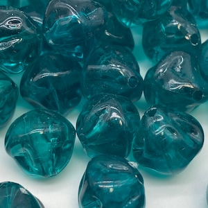 Puede incluir: Una colección de cuentas de vidrio azul turquesa con forma irregular facetada. Las cuentas son translúcidas y perfectas para la elaboración de joyas.