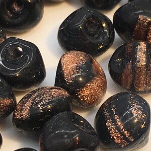 May include: Close-up of a collection of black glass beads with copper-colored glitter accents. The beads are smooth and rounded, with a glossy finish. These beads are suitable for jewelry making and crafting projects.