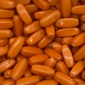 May include: A close-up image of a pile of orange oval-shaped beads. The beads are smooth and glossy.