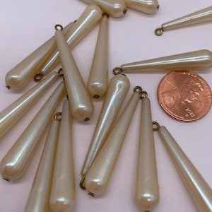 May include: A group of 16 off-white teardrop-shaped beads with gold-toned metal loops. The beads are approximately 1.5 inches long and are scattered on a white surface.