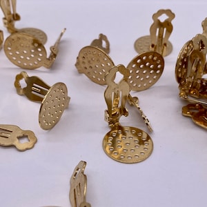 Op de afbeelding: Een groep gouden oorclips met een rond, geperforeerd ontwerp. De clips zijn ontworpen om op de oorlel te worden gedragen en hebben een veermechanisme om ze op hun plaats te houden.