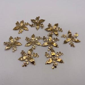 May include: Ten gold metal floral embellishments with a detailed leaf design. Each embellishment has a small hole in the center.