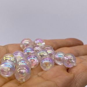 May include: A pile of iridescent clear glass beads in a hand. The beads are round and have a rainbow sheen.