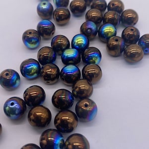 May include: A collection of iridescent brown glass beads with a blue and green shimmer. The beads are round and have a smooth surface.