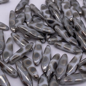 May include: A collection of white and silver glass beads with a speckled pattern. The beads are shaped like long, narrow ovals.