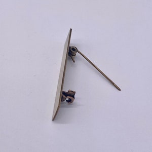 Pode incluir: Uma etiqueta de nome retangular de metal dourado, em branco, com um pino na parte de trás.