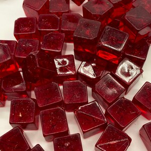May include: A collection of small, red, glass cubes. The cubes are translucent and have a slightly frosted appearance.