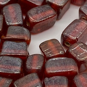 May include: Close-up of a collection of rectangular beads. The beads are a translucent reddish-brown color with a darker, smoky band across the center. The beads have rounded edges and a hole for stringing.