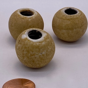 May include: Three small, round, ceramic vases with a speckled, light brown glaze and white interiors. The vases have a small opening at the top.