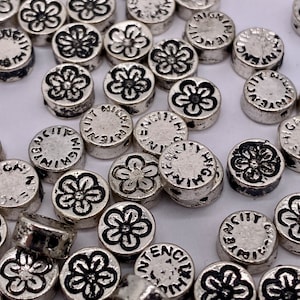 May include: A large quantity of silver-toned metal beads with a flower design and the words "INTENSITY" and "BY NIGHT" engraved on them.